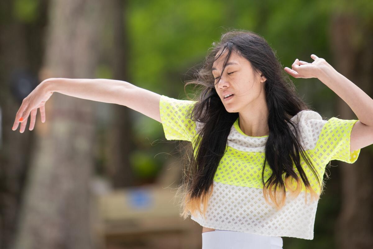 A woman with long dark hair closes her eyes and extends her arms.