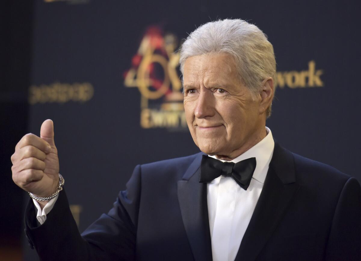 Alex Trebek gives a thumbs up with a look of assurance on his face while wearing a black tuxedo and bowtie 