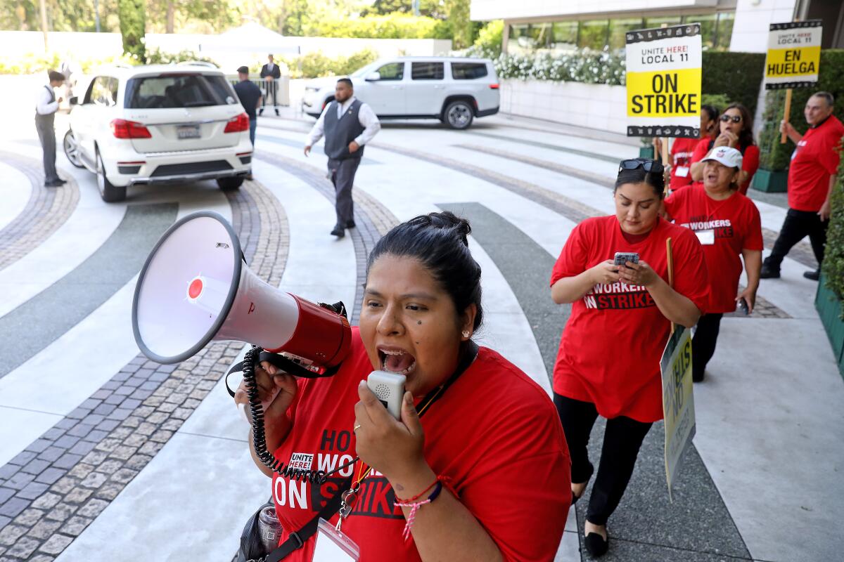 A woman leads a picket line while speaking into a megaphone. 