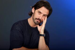 Milo Ventimiglia poses by resting his face on his opened hand, giving a slight smile