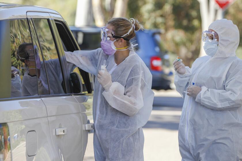 At a drive up testing site, Covid Clinic medical assistants Rhiannon Weik (left) and Arely Gutierrez (right) collect samples for Coronavirus COVID-19 testing at the San Elijo campus of Mira Costa College on April 15, 2020 in Cardiff, California.