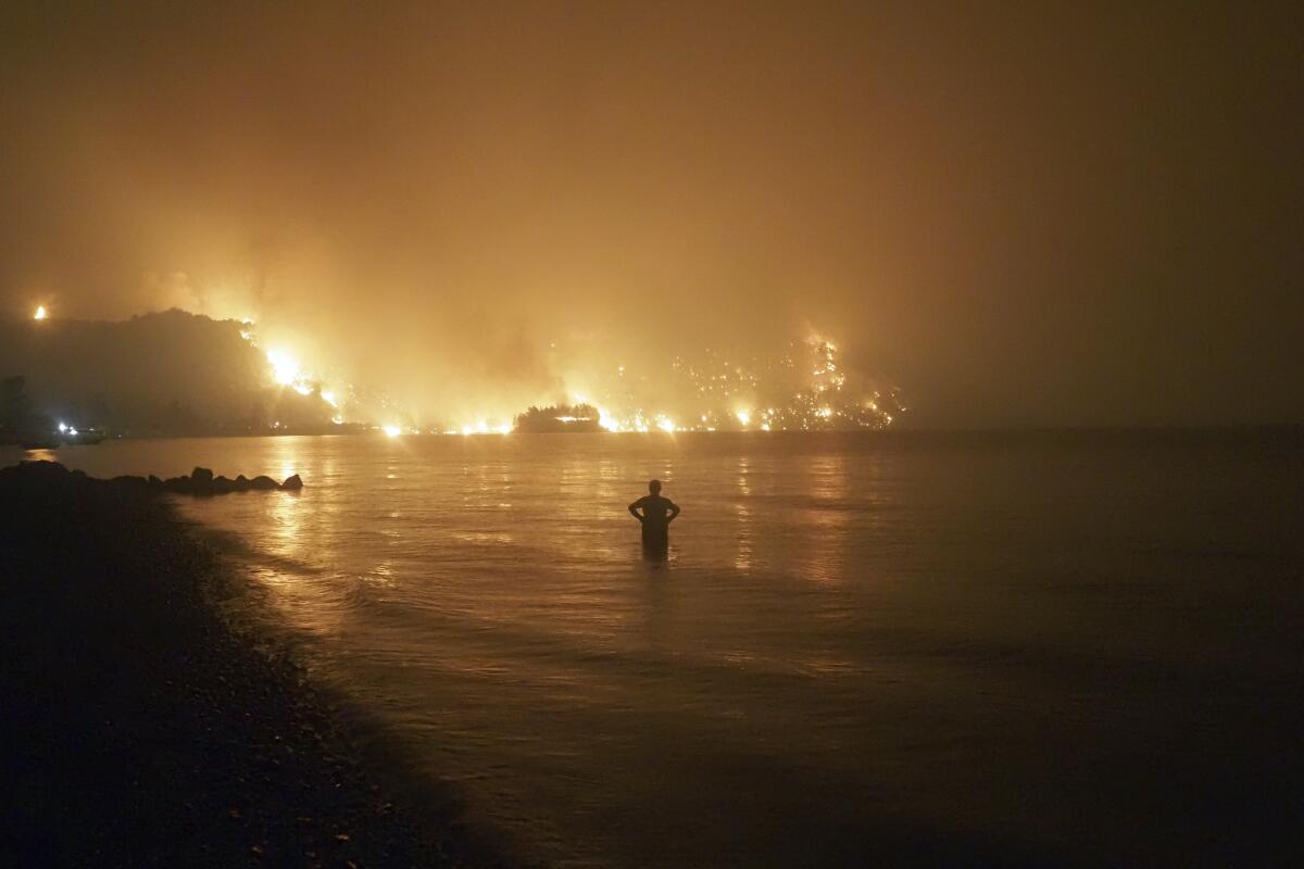 A person stands in the water watching a fire burn up the coast.
