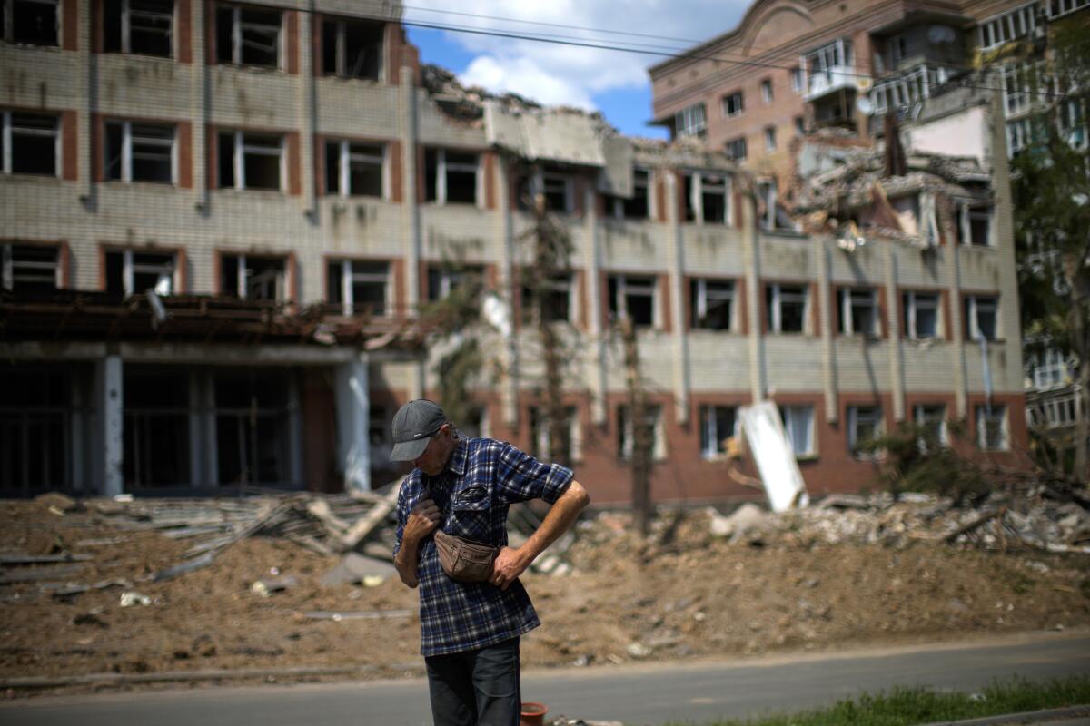 A person stands next to a building that has been heavily damaged by bombing.