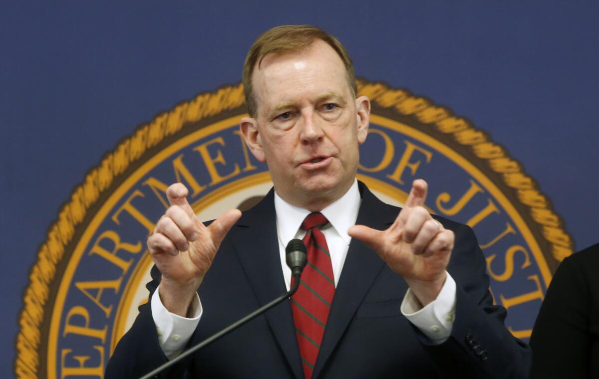 McGregor Scott at a news conference in Sacramento with the Department of Justice seal behind him.