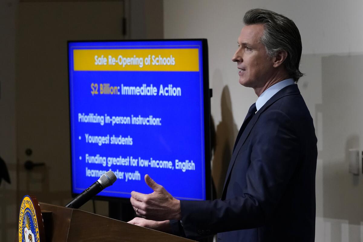 Gov. Gavin Newsom stands at a lectern as a TV shows his 2021-22 state budget proposal.