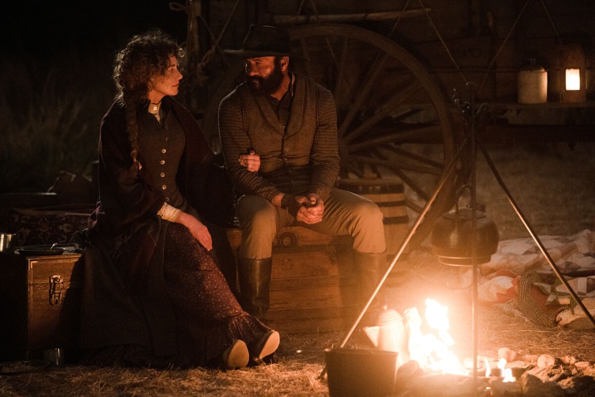 A man and woman in the old west sit beside a campfire in a scene from "1883."