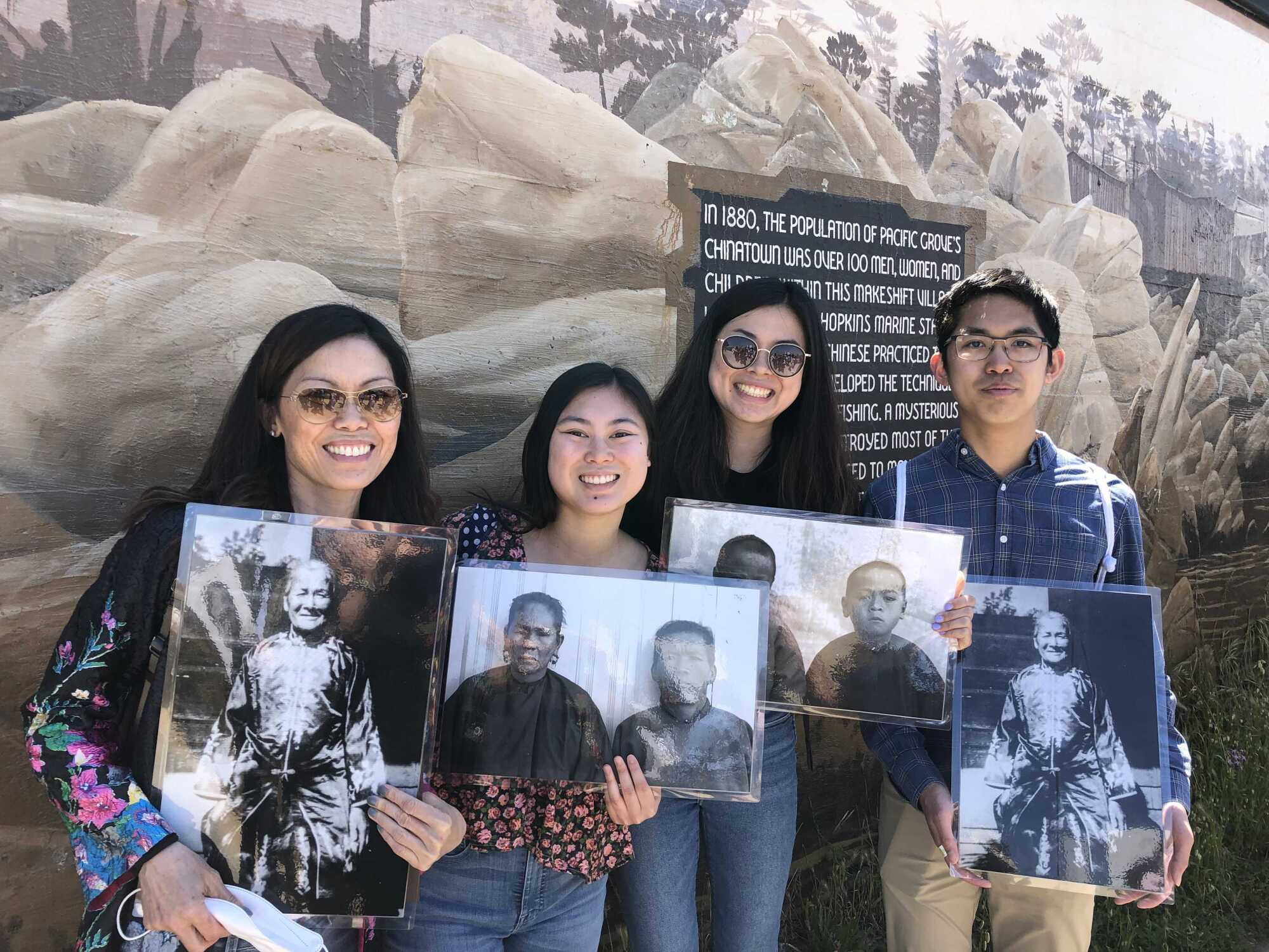 Four people standing in front of a mural on Pacific Grove's Chinatown, holding historic photos of people of Chinese descent.