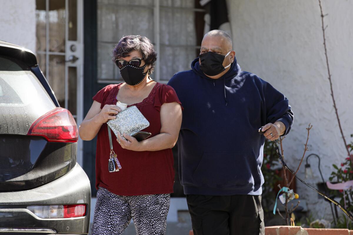 A man and woman in masks walk toward a car.