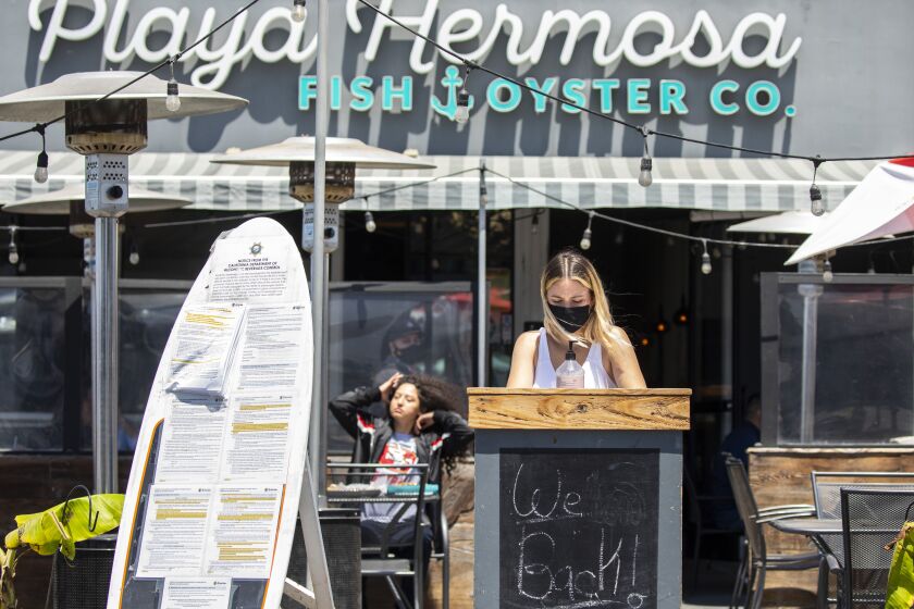 Hermosa Beach, CA - May 14: A masked hostess waits for customers at Playa Hermosa Fish & Oyster Co., on Hermosa Plaza, in Hermosa Beach, CA, a day after the Centers for Disease Control and Prevention (CDC) loosened guidelines for vaccinated people, with masks no longer being necessary when outdoors or in most indoor situations, Friday, May 14, 2021. The new guidelines state that fully vaccinated people no longer need to wear a mask or physically distance in any setting, except where required by federal, state, local, tribal, or territorial laws, rules, and regulations, including local business and workplace guidance. (Jay L. Clendenin / Los Angeles Times)