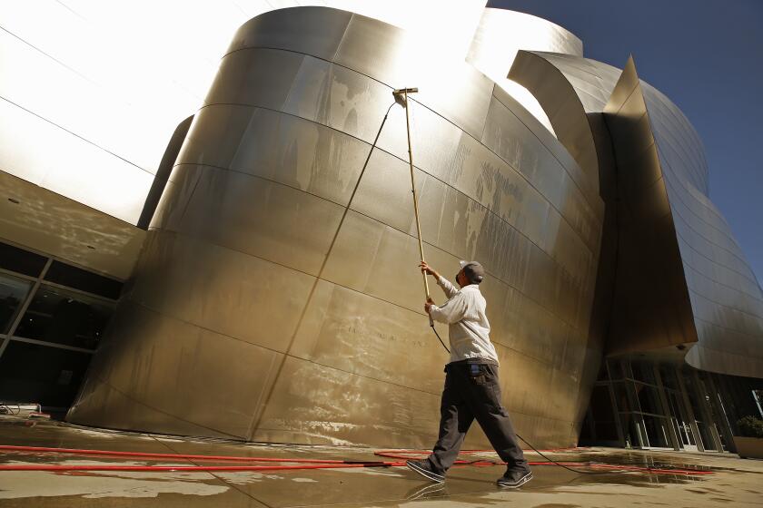 LOS ANGELES, CA - MARCH 22: Alex Espadero with Sunrise Window Cleaning uses a special extension wand to clean the metal of Walt Disney Concert Hall on Monday March 22, 2021. The 179,150 square feet of metal is cleaned once a year but takes over one month to complete the cleaning. 45 percent of the building is cleaned by workmen on a scaffold but the remaining 55 percent is by hand using the special wand using ionized water. Regular water would leave stains. The first 4 panels up from the ground are cleaned 34 times a week sometimes using joy soap to get the finger prints off. The cleaning is usually in preparation for the Los Angeles Philharmonic summer opening but plans for 2021 remain on hold due to COVID-19. Disney Hall on Monday, March 22, 2021 in Los Angeles, CA. (Al Seib / Los Angeles Times).