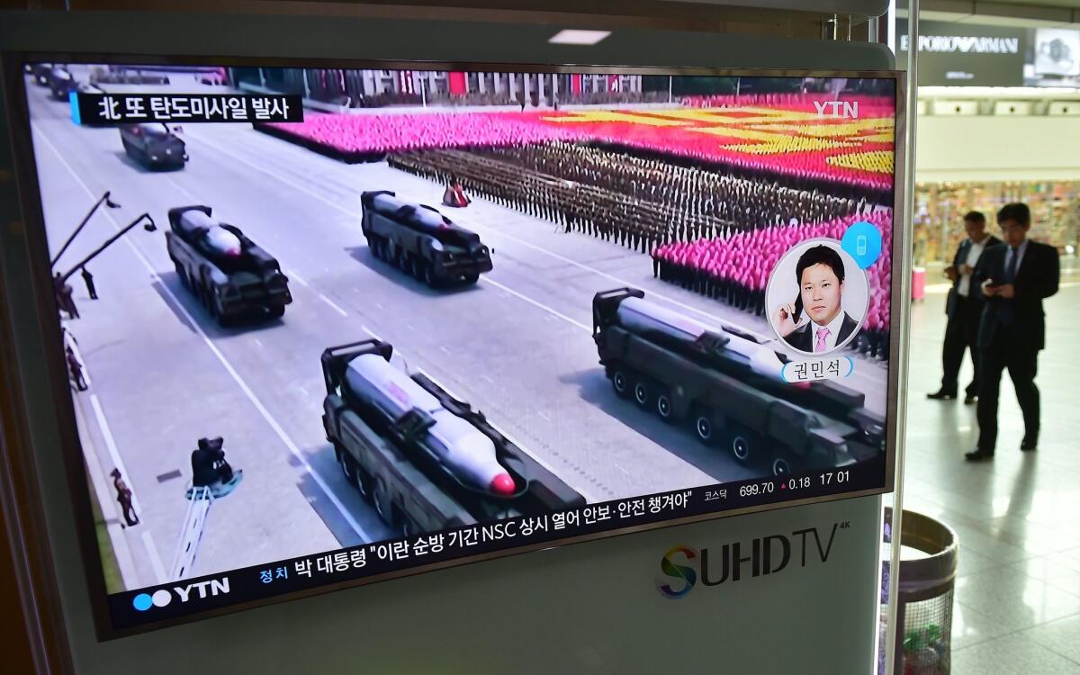 Railway travelers in a Seoul station pass a TV screen showing North Korean missiles.