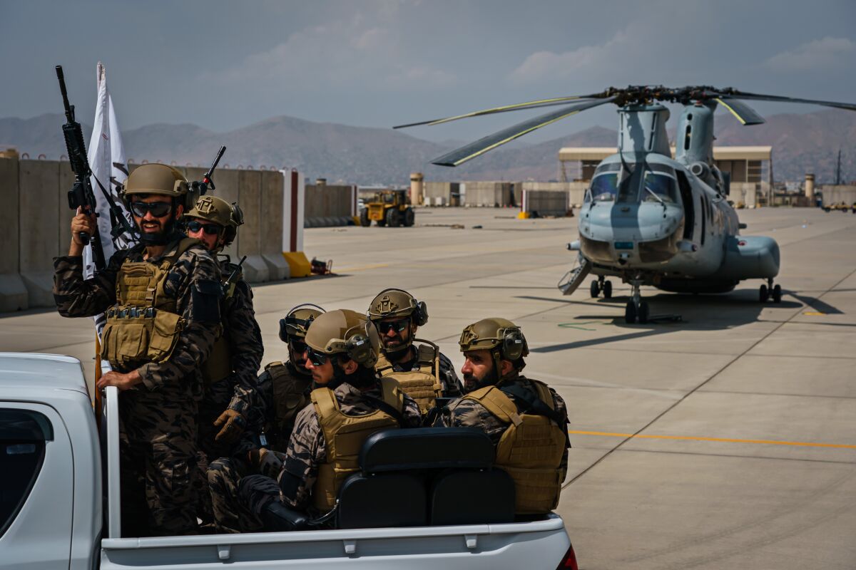 Armed Taliban fighters ride in a truck past a helicopter left at Hamid Karzai International Airport in Kabul.