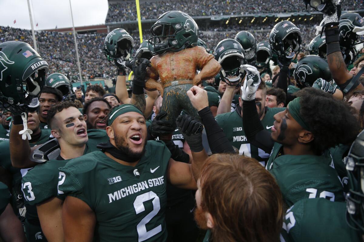 Michigan State players celebrate with the Paul Bunyan trophy after defeating Michigan.