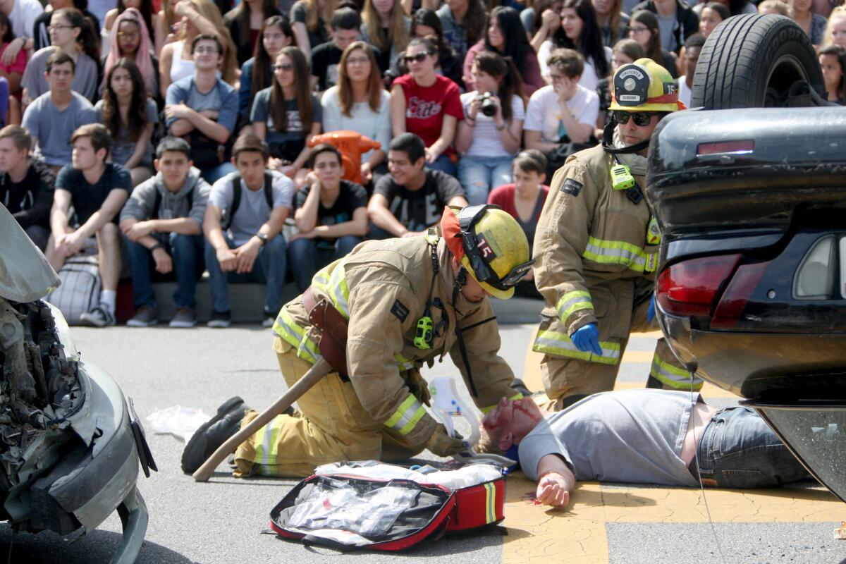 During the "Every 15 Minutes" simulation, students watch as Burbank Fire Department personnel tend to mock-accident victim Randy Tobin in front of Burroughs High School, in Burbank on Thursday, April 21, 2016. "Every 15 Minutes" is a program with real cars, police, fire and coroner department personnel and students who act out a scene of a multiple-vehicle accident with fatalities, all with the goal of warning students of the dangers of drunk driving.