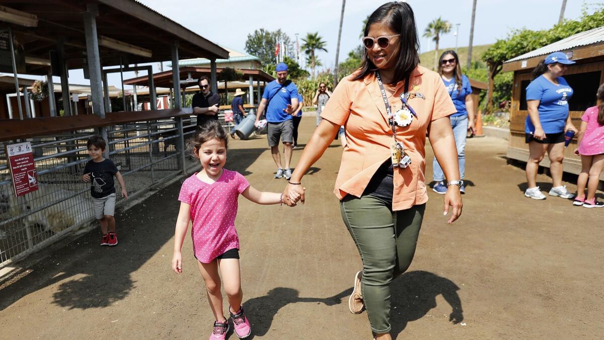 Sabrina Simoes, 5, holds hands with Centennial Farm supervisor Evy Young as Sabrina and her family meet animals Friday at the OC Fair & Event Center in Costa Mesa. The Orange County Fair and Make-A-Wish granted Sabrina's wish for an outdoor adventure.