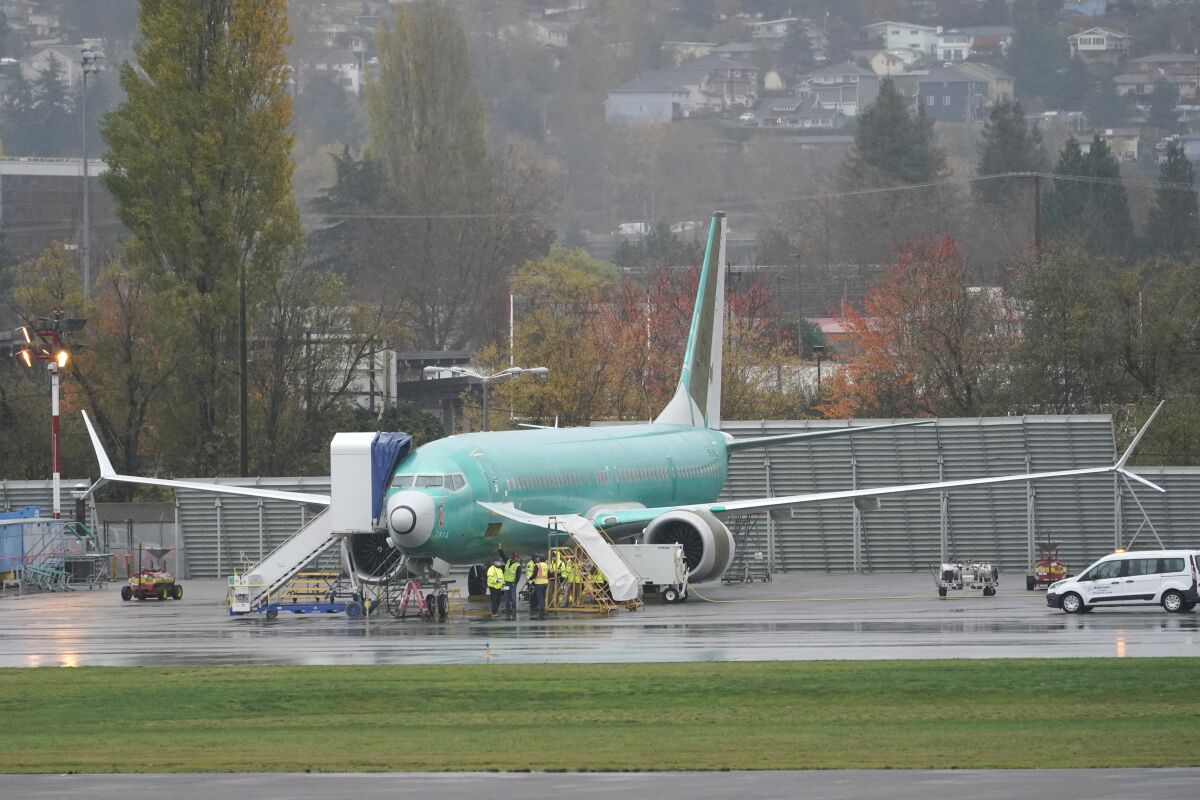 FILE - In this Wednesday, Nov. 18, 2020 file photo, workers stand near a Boeing 737 Max airplane parked at Renton Municipal Airport next to the Boeing assembly facility in Renton, Wash., where 737 Max airplanes are made. On Tuesday, Jan. 12, 2021, the company reported final 2020 numbers for airplane orders and deliveries, and they are down from 2019 even though the 737 Max is flying again. (AP Photo/Ted S. Warren)