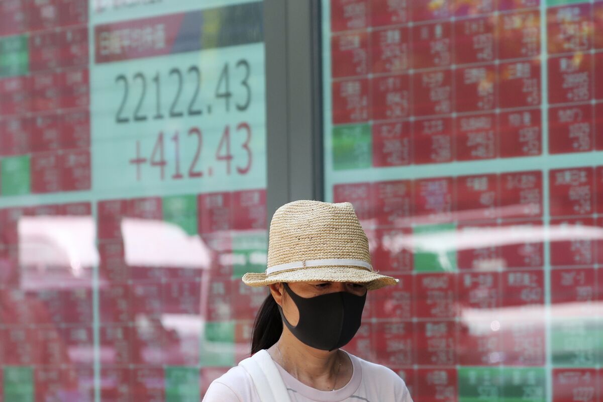 FILE - In this Aug. 3, 2020, file photo, a woman wearing a face mask walks by an electronic stock board of a securities firm in Tokyo. Shares advanced in Asia on Tuesday, Aug. 11, extending another rally that took the S&P 500 to within striking distance of its all-time high set in February. (AP Photo/Koji Sasahara, File)