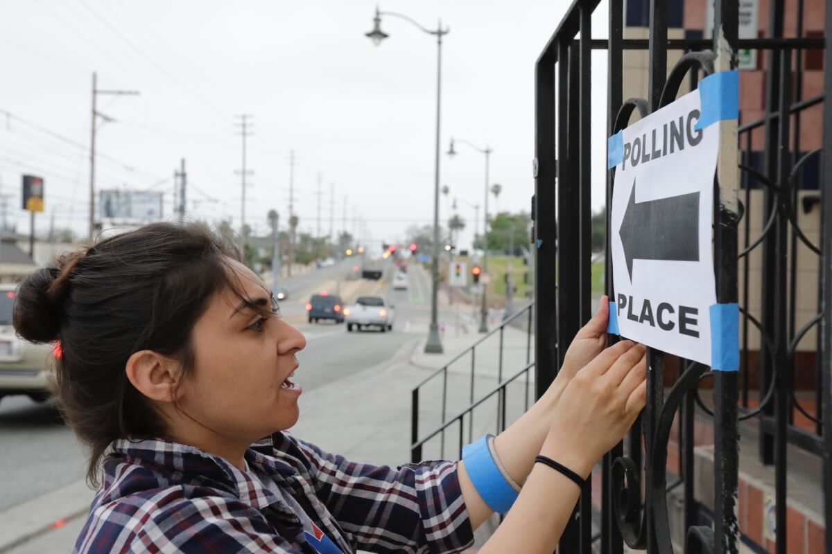 Poll worker Shannon Diaz puts up signs as voting begins at El Mercado de Los Angeles in Boyle Heights on Tuesday.