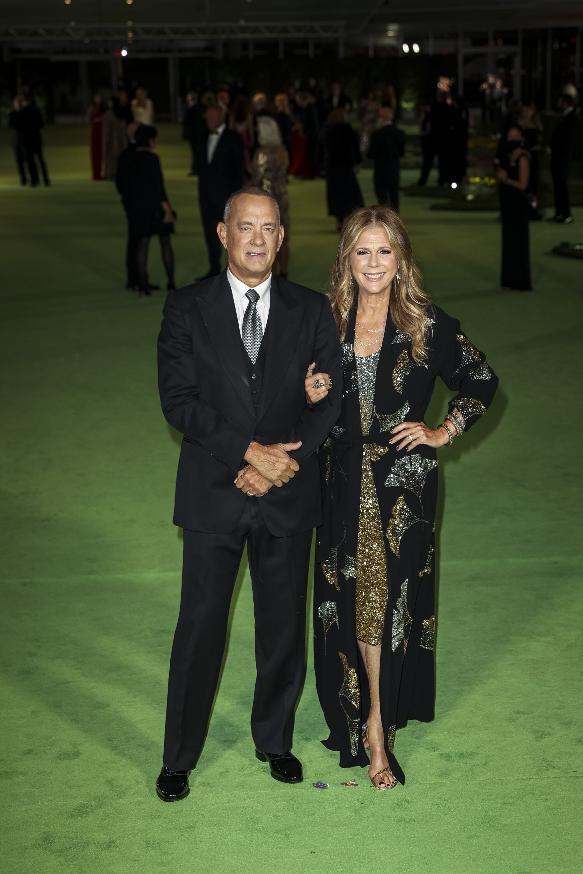 A man in a black suit and a woman in a sparkly gown posing on the green carpet