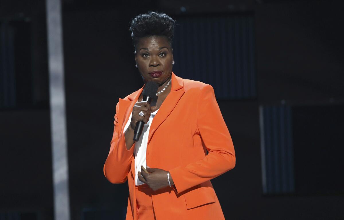 A woman in an orange suit speaking into a mic. 