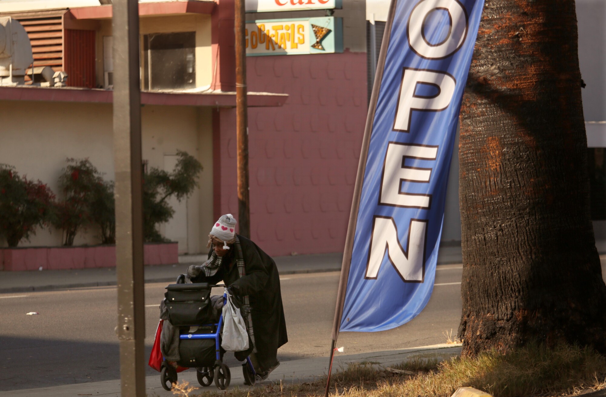 A homeless woman pushing her belongings as a sign declares that it's still open for business in Stockton.