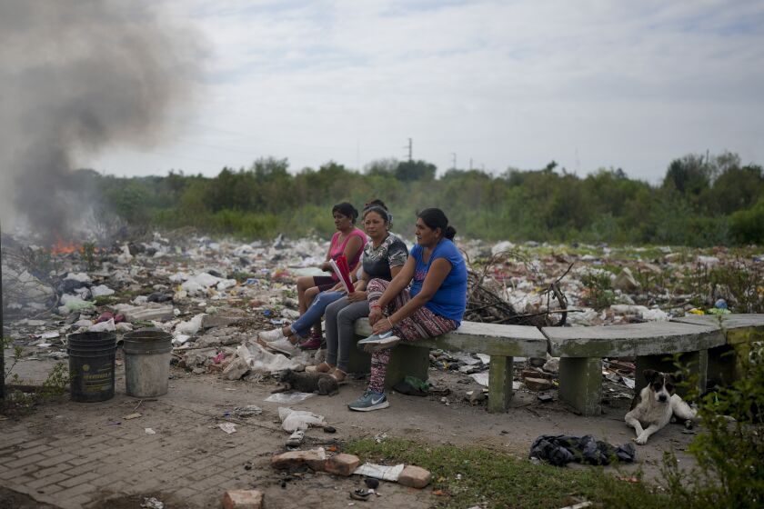 Women sit on a bench where garbage is tossed, near their homes in Tucuman, Argentina, Thursday, March 30, 2023. (AP Photo/Natacha Pisarenko)