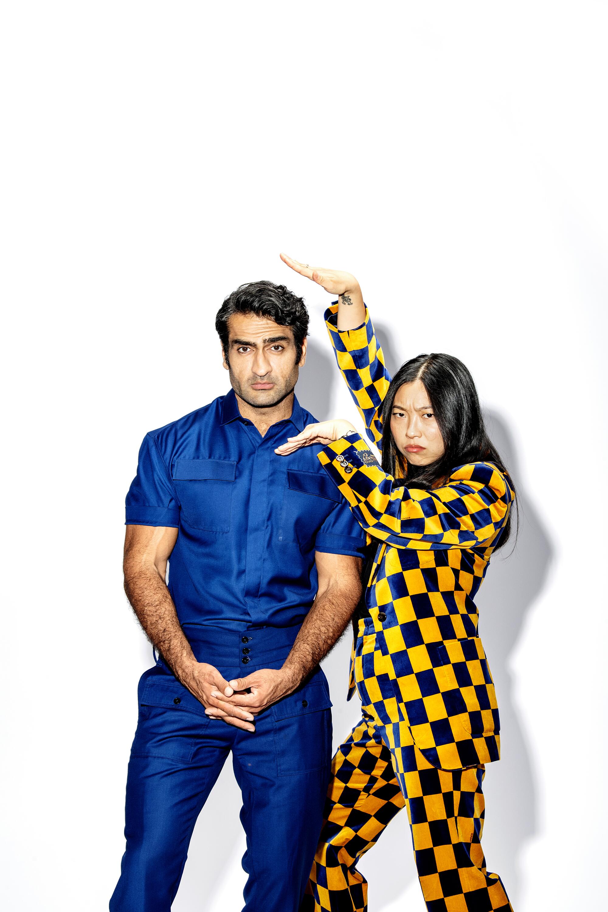 A man with dark hair in a blue outfit, left, stands next to a woman in a yellow-and-black checkered suit striking a pose 