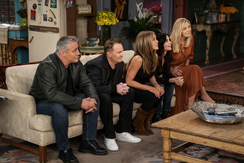 The cast of "Friends" on a couch in the series' apartment set playing a game