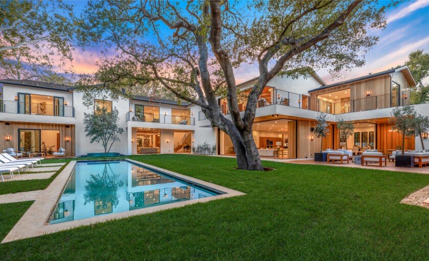 A rectangular pool in a big yard in front of a sprawling mansion.