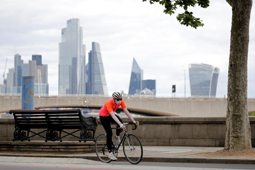 A man wearing PPE (personal protective equipment), including a face mask as a precautionary measure against COVID-19, cycles along Embankment, backdropped by the skyscrapers and office buildings of the City of London, on May 13, 2020, as people start to return to work after COVID-19 lockdown restrictions were eased. - Britain's economy shrank two percent in the first three months of the year, rocked by the fallout from the coronavirus pandemic, official data showed Wednesday, with analysts predicting even worse to come. Prime Minister Boris Johnson began this week to relax some of lockdown measures in order to help the economy, despite the rising death toll, but he has also stressed that great caution is needed. (Photo by Tolga AKMEN / AFP) (Photo by TOLGA AKMEN/AFP via Getty Images)