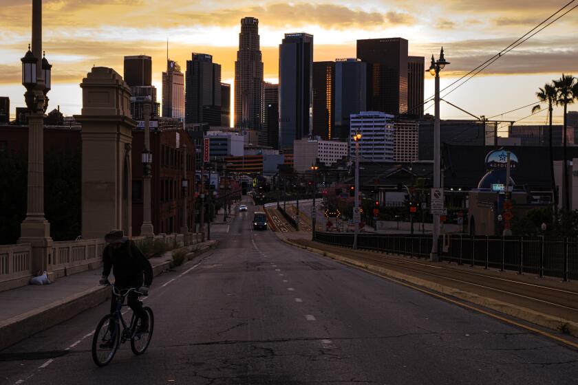 LOS ANGELES, CALIF. -- MONDAY, APRIL 6, 2020: The sun sets as a lonely figure cycles up First Street Bridge, towards Boyle Heights as the silence reign supreme over downtown Los Angeles, Calif., on April 6, 2020. In California, there are more than 16,363 confirmed COVID-19 cases, according to a tally maintained by the Los Angeles Times. At least 387 have died. (Marcus Yam / Los Angeles Times)