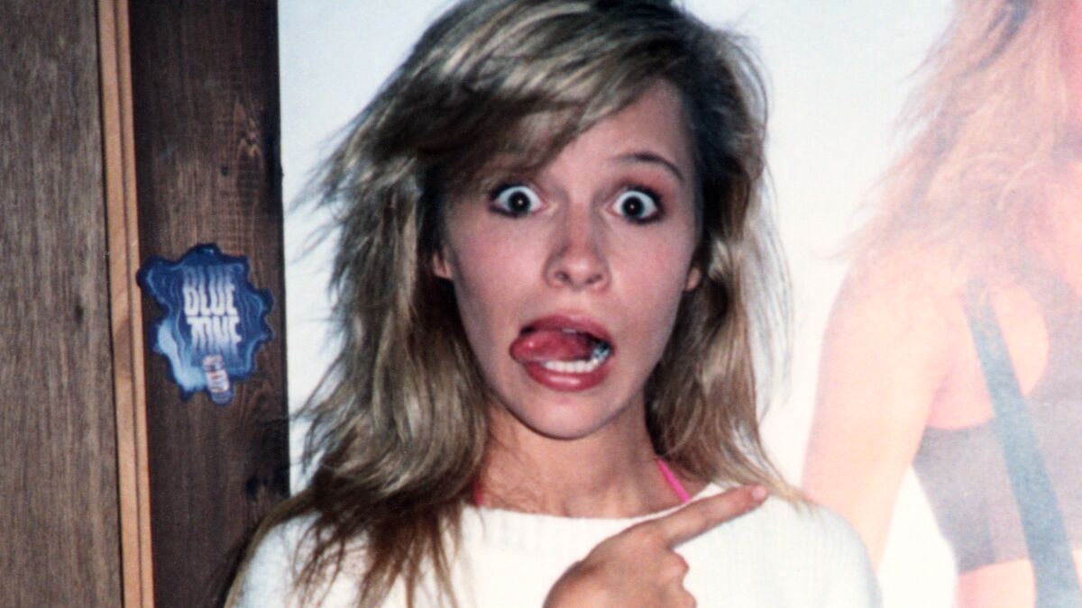 Pamela Anderson points to a poster of herself in a moment from "Pamela, a Love Story."