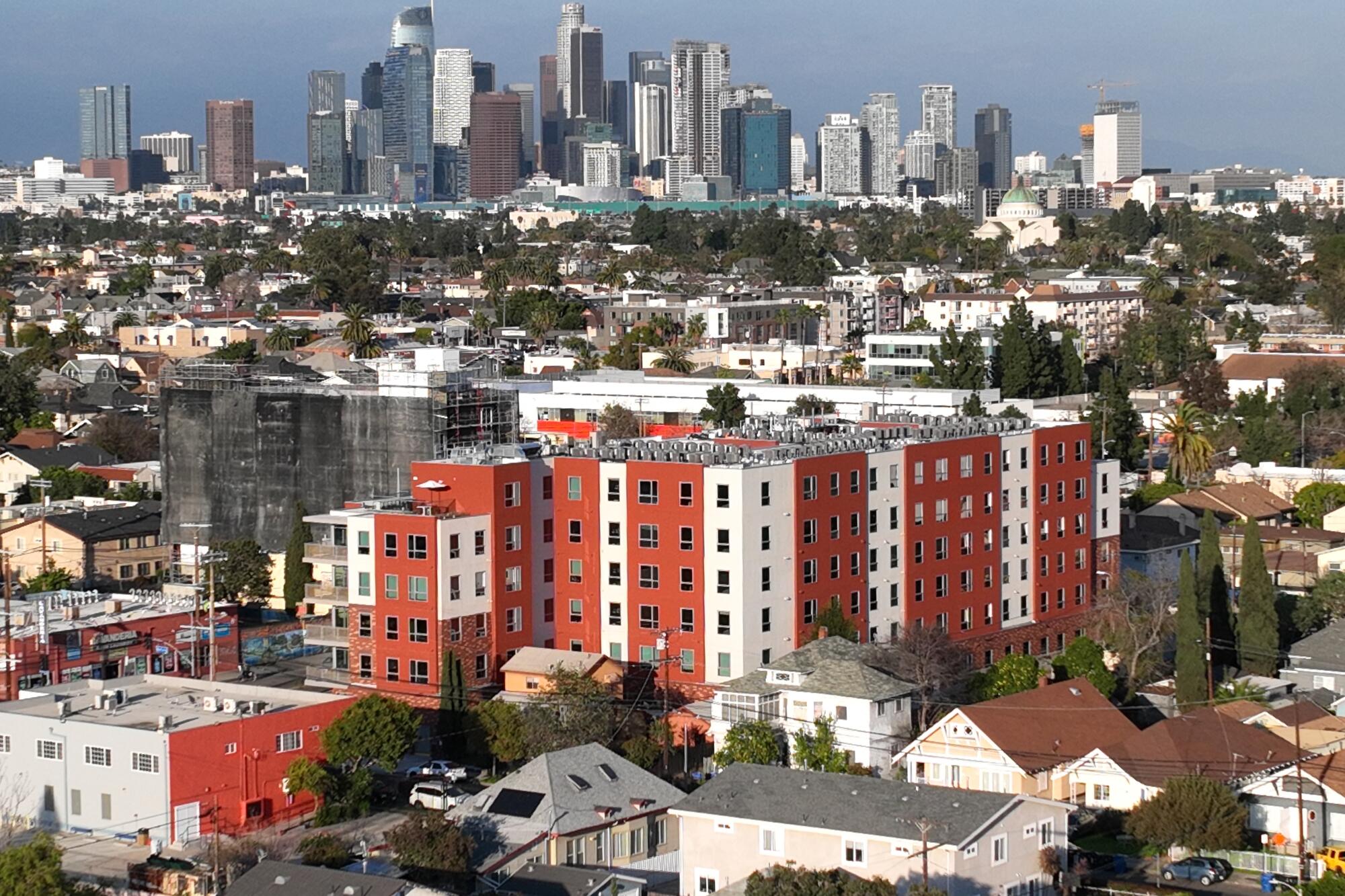 Brightly colored red and white apartments surrounded by homes, with a city skyline in the distance
