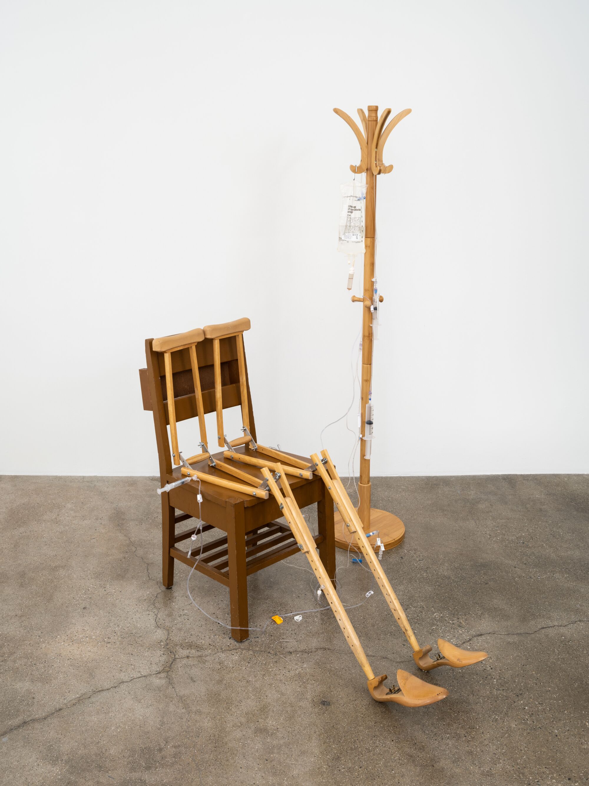 An artwork by Panteha Abareshi of a wooden figure on a chair, hooked up to an IV.