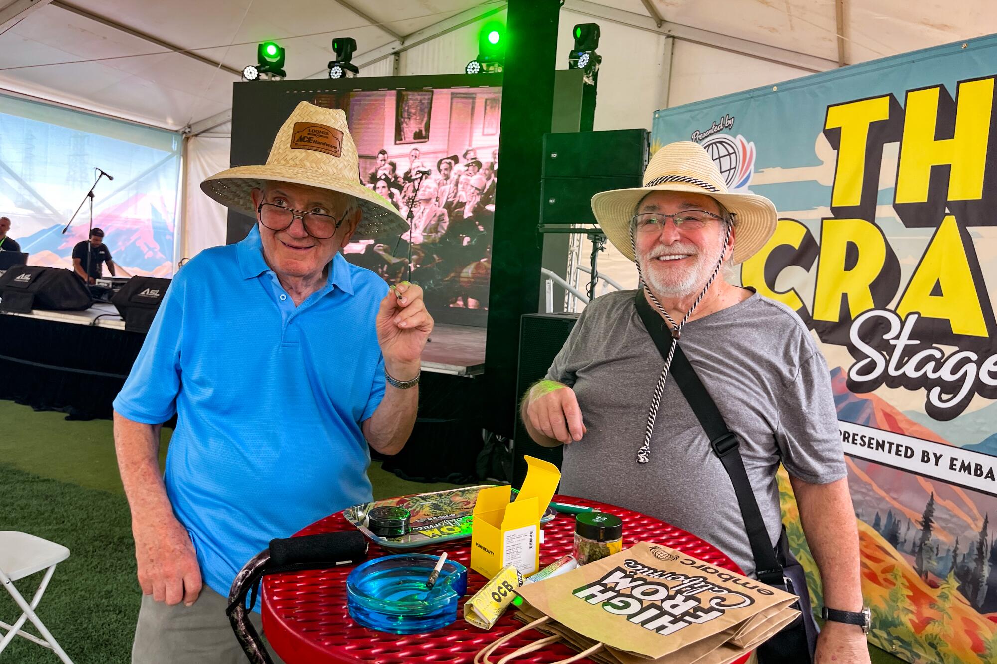 Two men in straw hats smiling and smoking a joint.