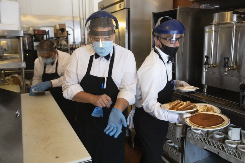 LOS ANGELES, CA - JULY 01, 2020: Waiter Jesus Segura, left, puts on gloves as waiter Alex Ortiz, passes by with breakfast plates for dine in customers at The Original Pantry in Downtown Los Angeles. The restaurant stopped dine in service soon after as a result of California Gov. Gavin Newsom announcing today that for the next 3 weeks, restaurants in Los Angeles County and a number of other counties statewide will only be allowed to have take out and delivery service due to an increase in coronavirus cases. (Mel Melcon / Los Angeles Times)
