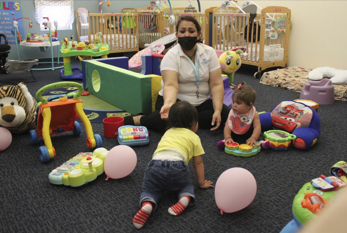 This May 4, 2021 image shows teacher Graciela Olague-Barrios working with two infants at Cuidando Los Ninos in Albuquerque, N.M. The charity provides housing, child care and financial counseling for mothers, all of whom will benefit from expanded Child Tax Credit payments that will start flowing in July to roughly 39 million households. (AP Photo/Susan Montoya Bryan)