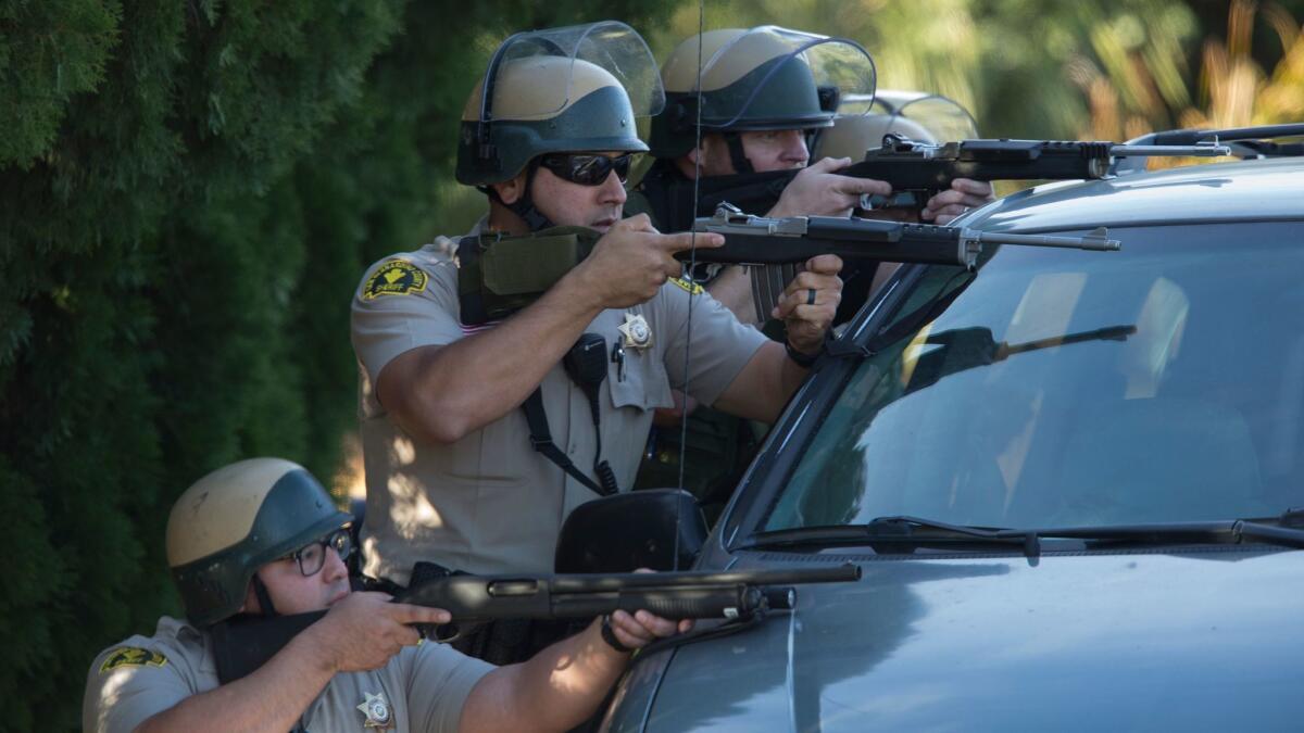 Sheriff's deputies crouch behind a minivan during a search for the assailants in the December 2015 mass shooting in San Bernardino.
