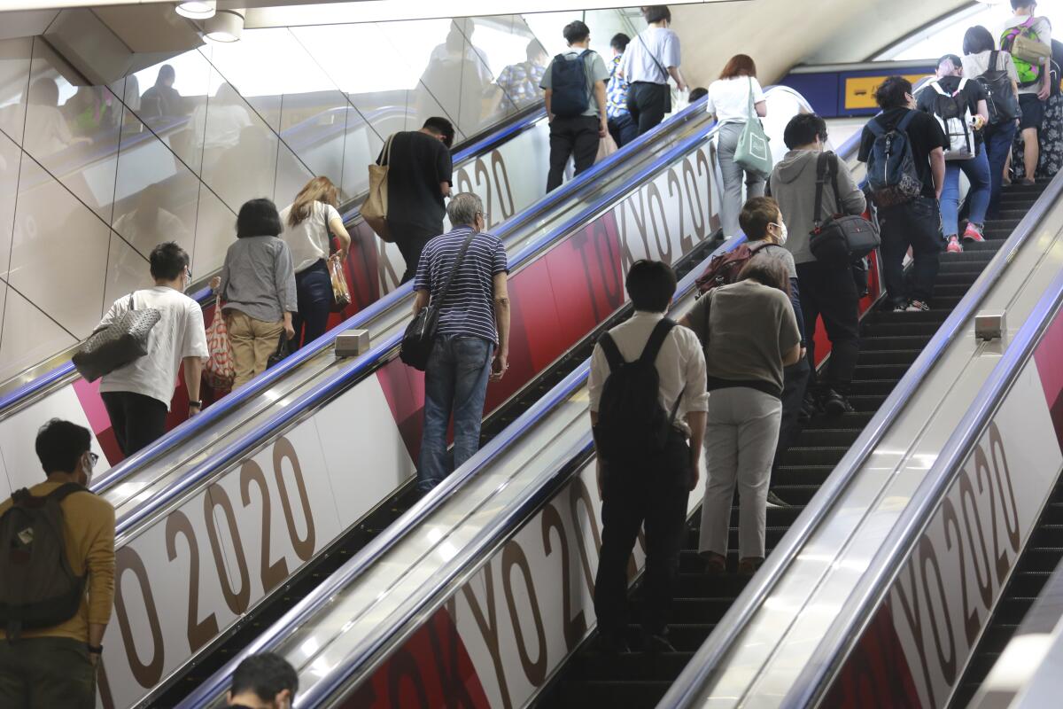 People in Tokyo ride escalators with banners July 6 to promote the upcoming Olympics Games.