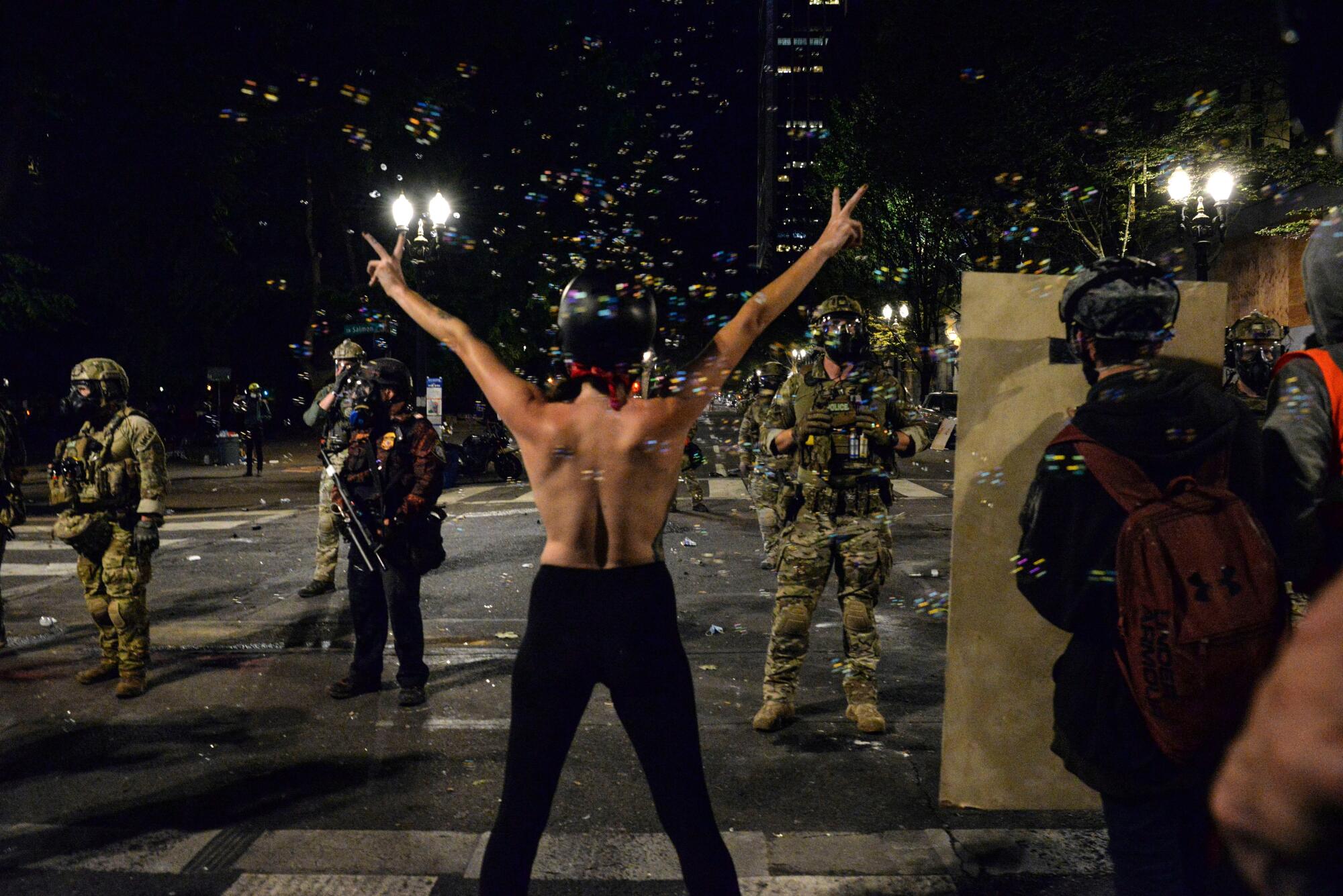 A topless protester gestures in front of federal police personnel in Portland, Ore.