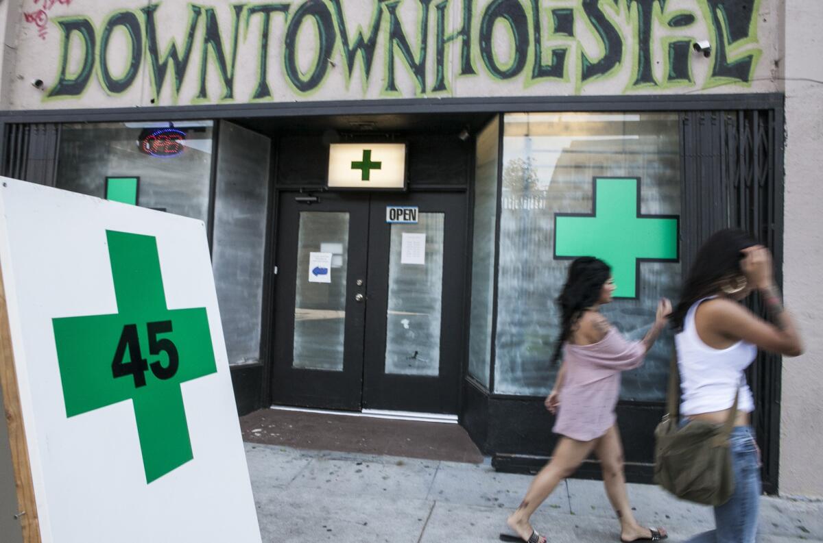 Pedestrians walk past a medical marijuana business in the Echo Park area of Los Angeles in 2012. The L.A. City Council is trying to implement a voter-approved measure to limit the number of pot shops.