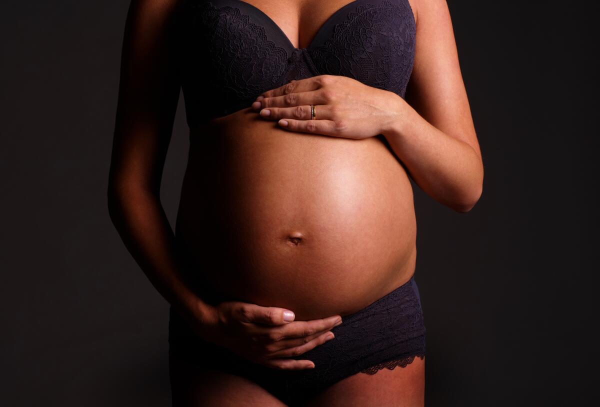 A pregnant woman holds her belly, with one hand on top and one below.