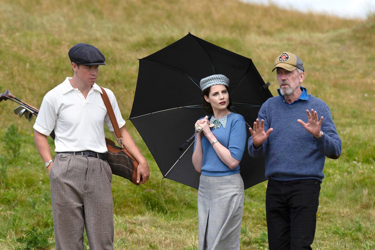 A man gestures instructions to a golfer and a woman holding an umbrella.