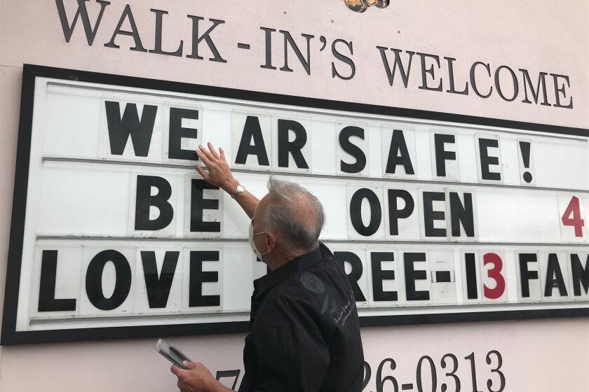 Lester Crowell, the owner of the Three-13 Salon, Spa and Boutique in Marietta, Ga., changes the lettering on a marquee outside his store to alert passers-by that his salon has re-opened. (Jenny Jarvie / Los Angeles Times)