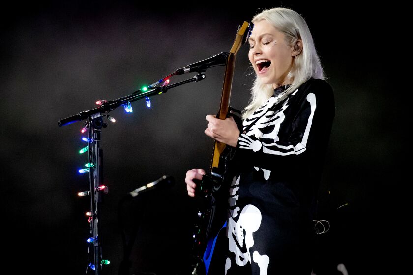 A blond woman in a skeleton costume playing guitar and singing into a microphone