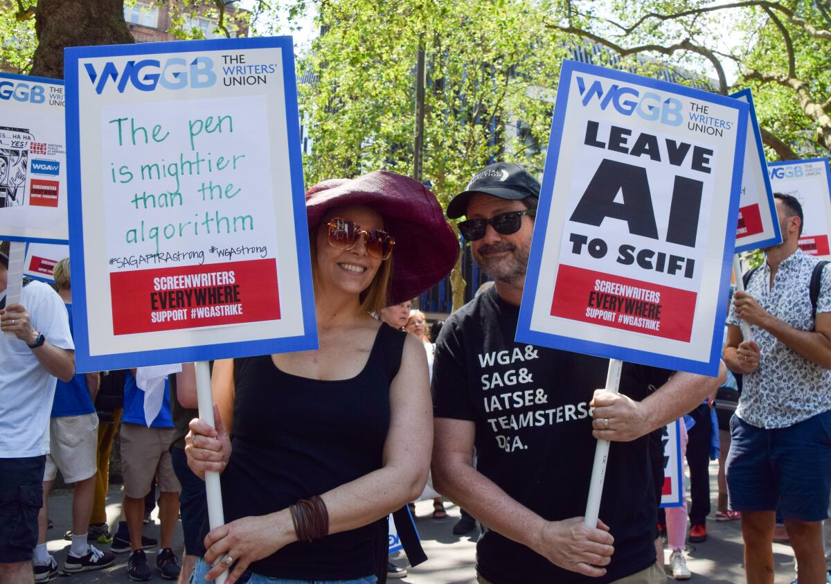 Protesters supporting the Writers Guild hold signs reading 'The pen is mightier than the algorithm' and 'Leave AI to sci-fi.'