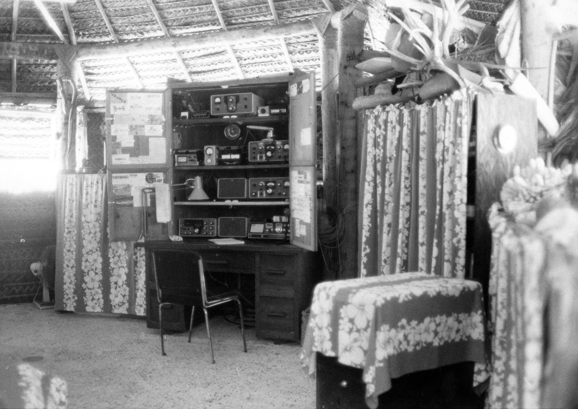 A bungalow holds a desk and shelves filled with ham radio equipment.