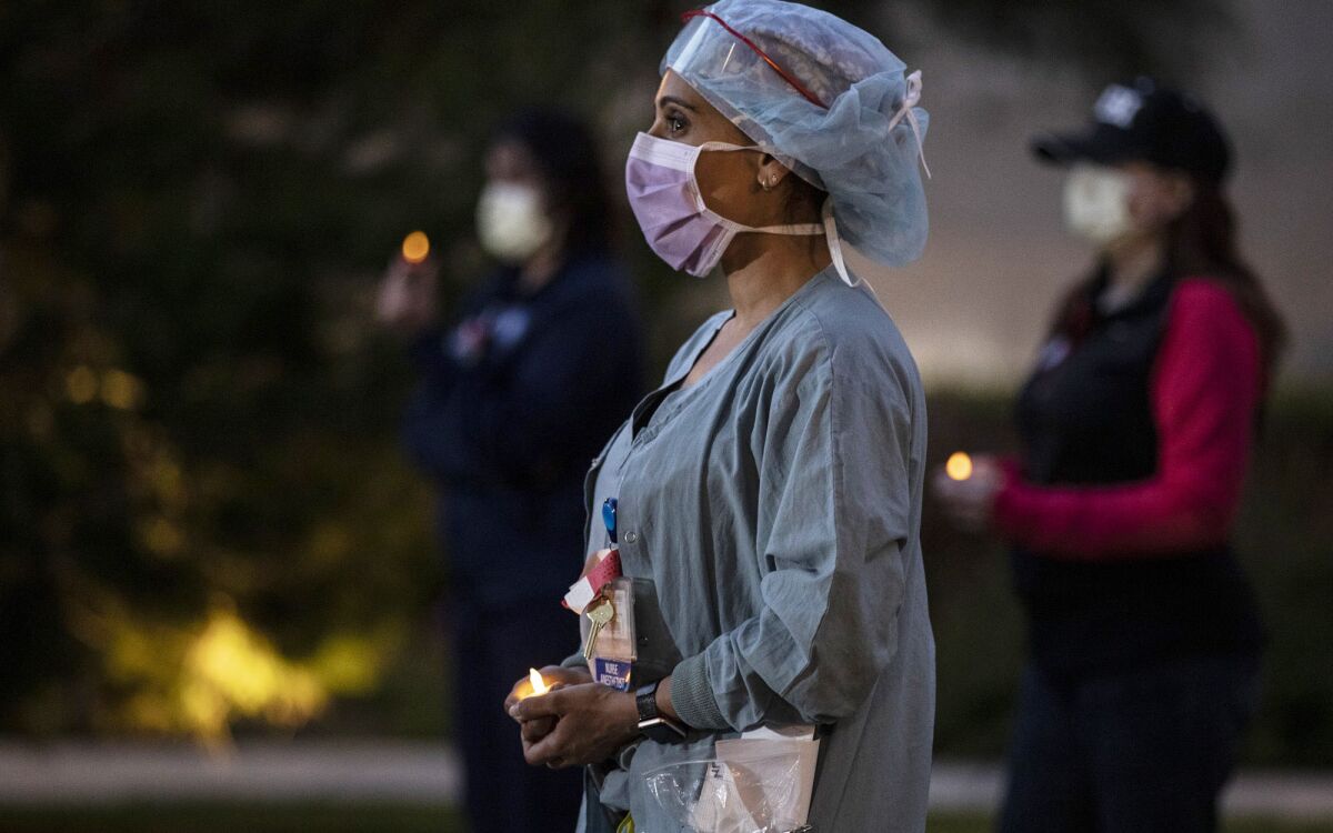 A healthcare worker in protective gear holds a candle at a vigil.