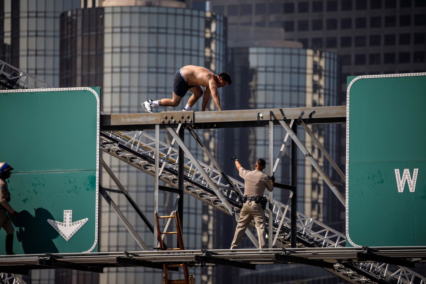 California Highway Patrol officers attempt to remove a shirtless man who scaled a freeway sign and shut down the southbound 110 Freeway in downtown Los Angeles.