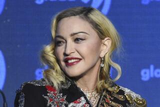 Madonna in a bejeweled black jacket looking over her right shoulder and smiling